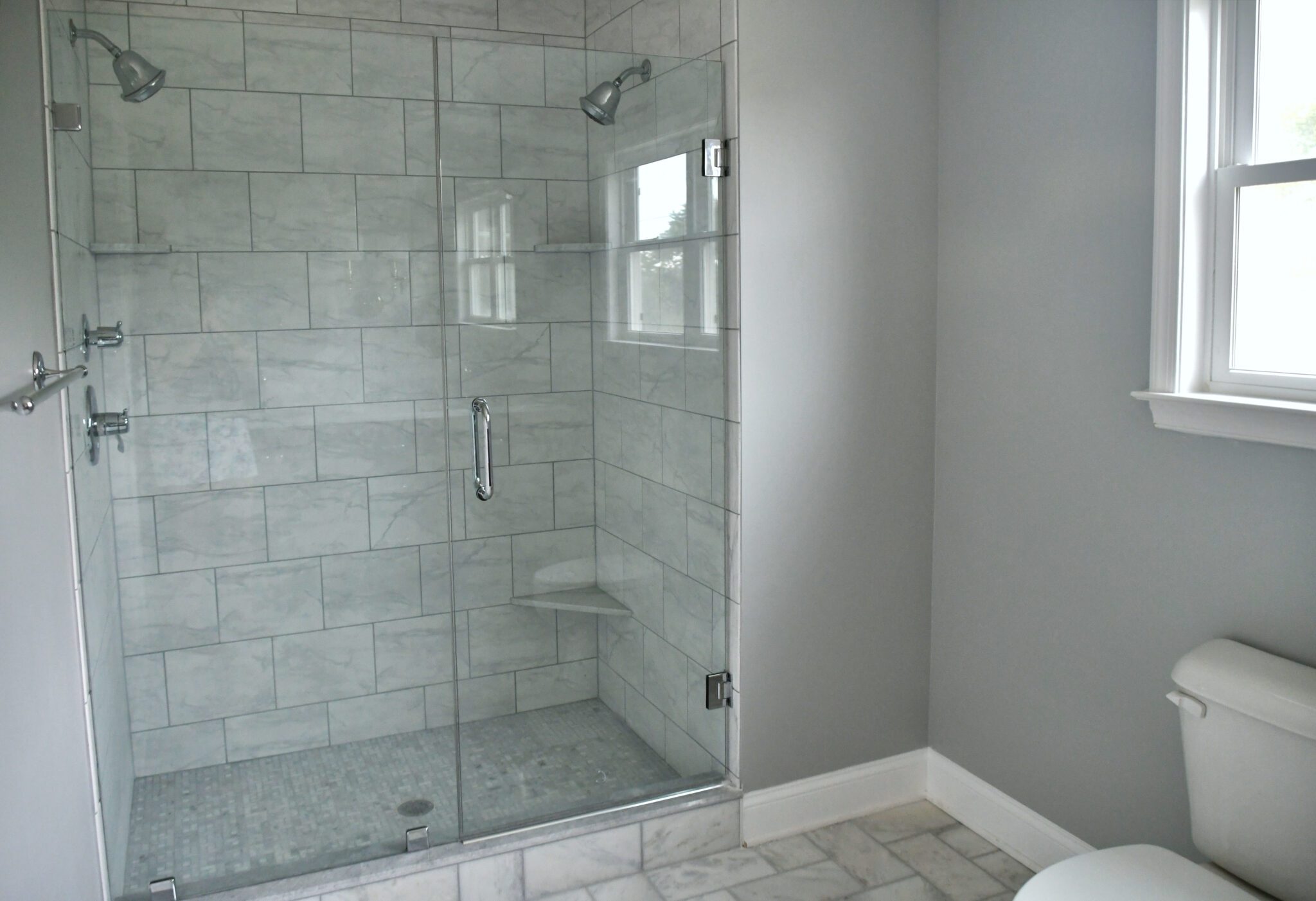 White and gray tile bathroom with new shower glass and silver hardware